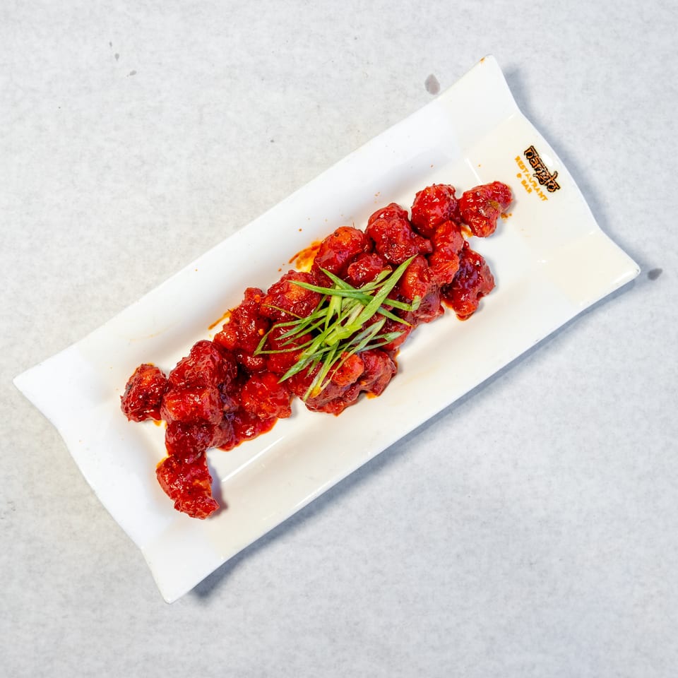 Glazed red meatballs topped with sliced green onions on a white rectangular plate.