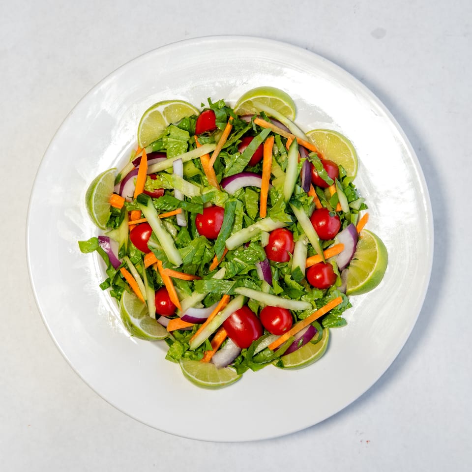 Fresh garden salad with lettuce, cherry tomatoes, cucumber, carrots, red onion, and lime wedges on a white plate.