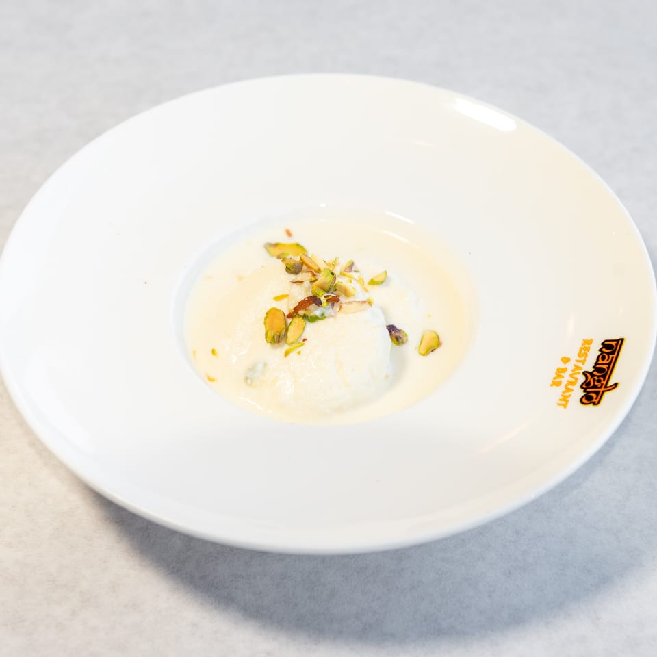 Creamy Indian dessert topped with pistachios, served on a branded white plate.