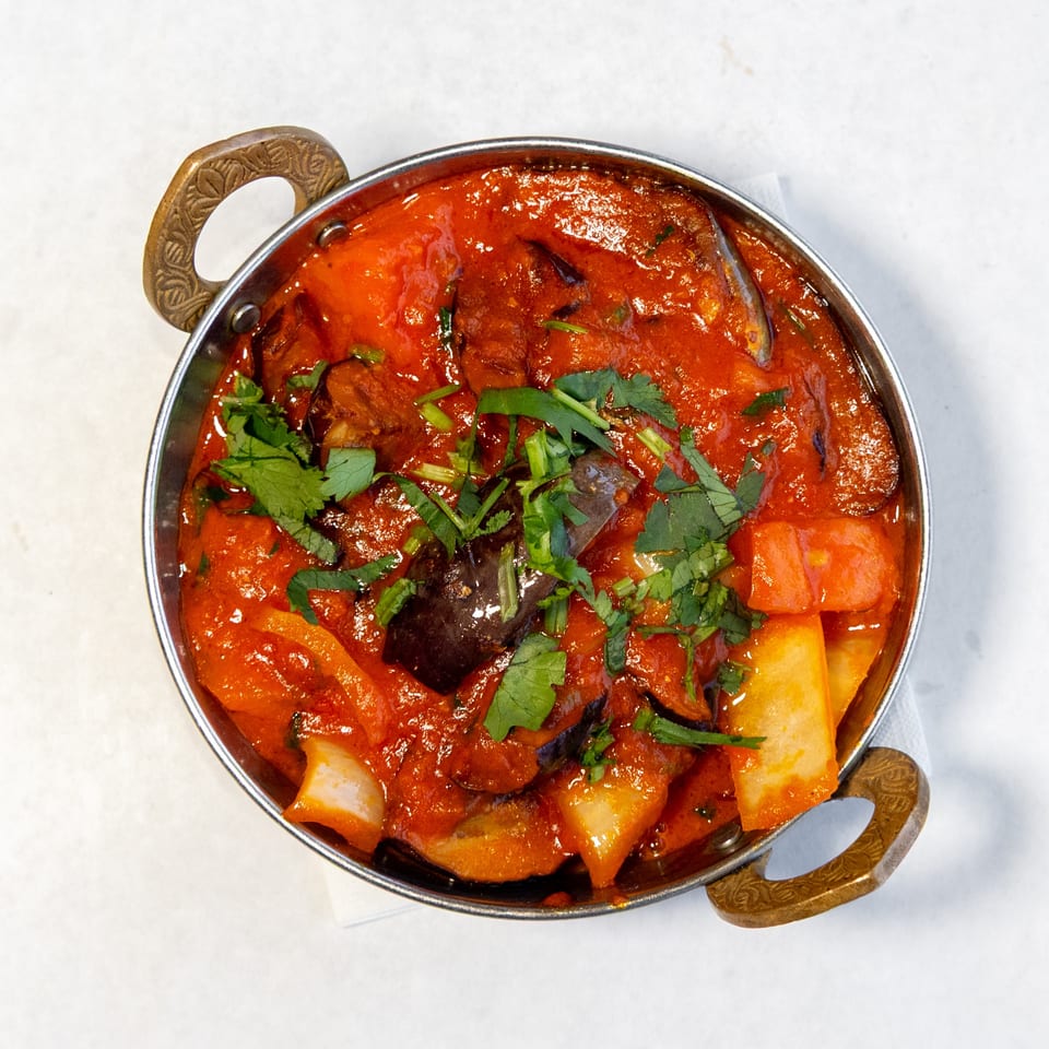 Overhead view of a metal serving dish filled with vegetables in rich red curry sauce, garnished with fresh cilantro.