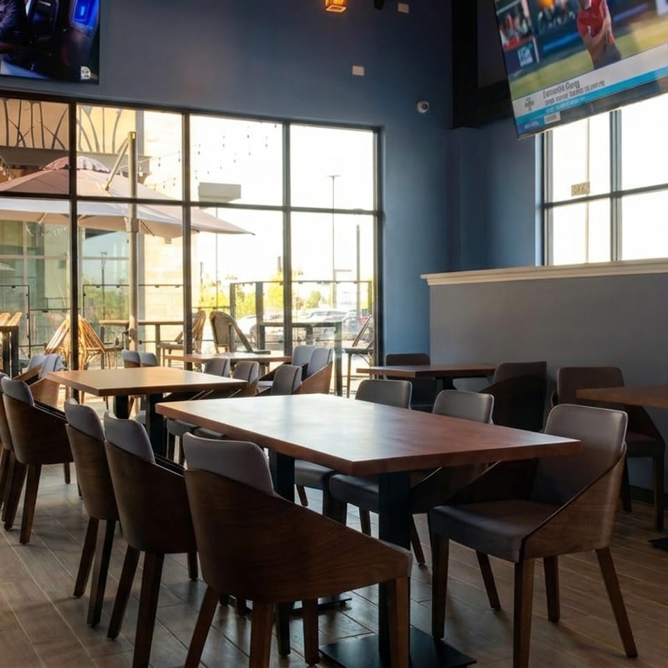 Restaurant interior with wooden tables and chairs, large windows, and a TV showing sports.
