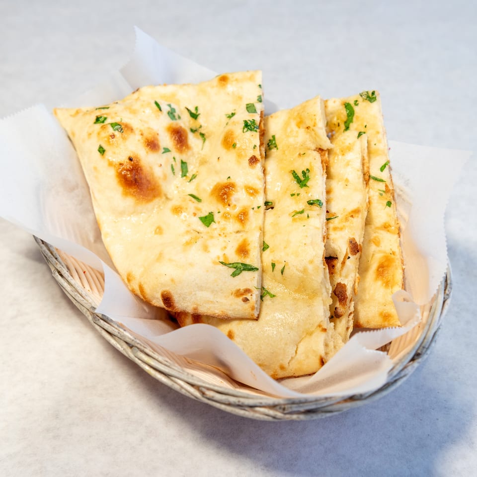 Basket of warm, golden flatbread pieces garnished with chopped parsley.