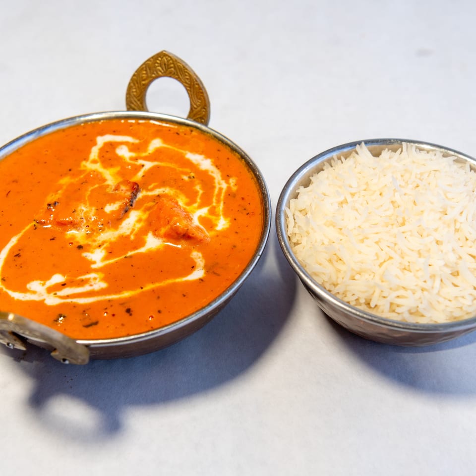 Indian butter chicken in creamy tomato curry served beside a bowl of white basmati rice in metal dishes.