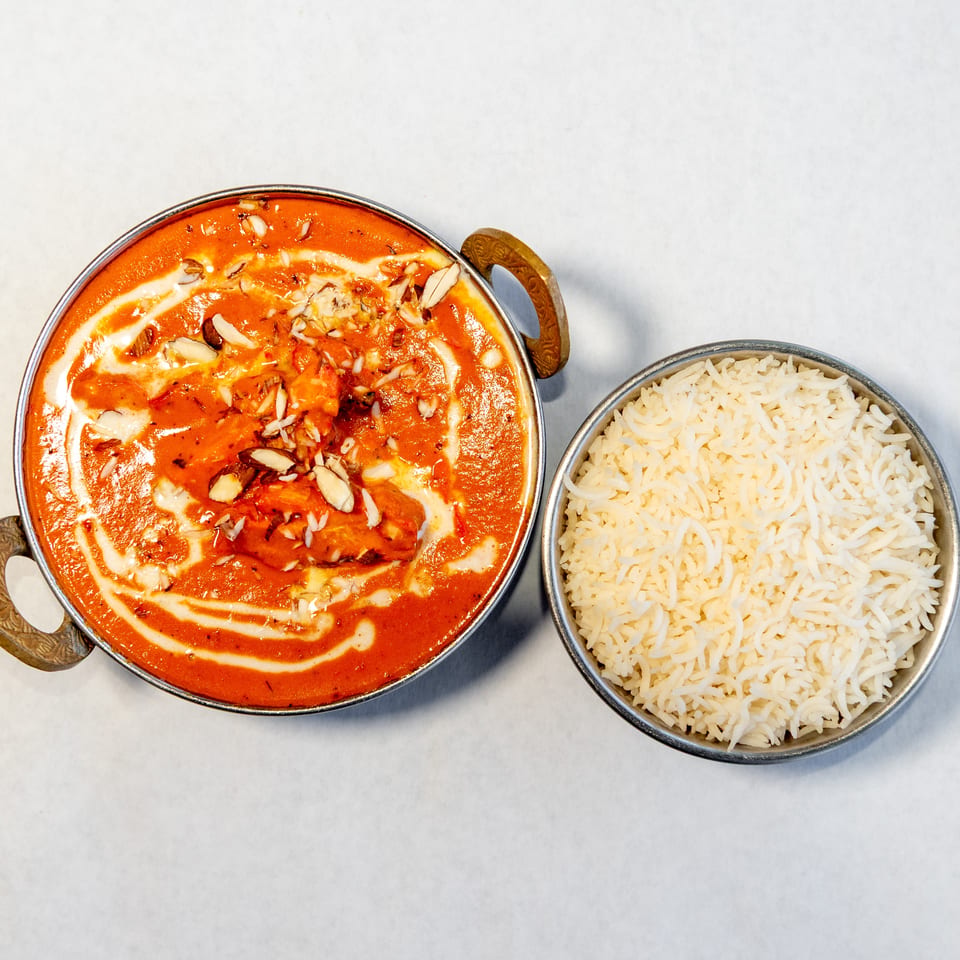 Creamy orange curry garnished with sliced almonds and cream, served beside a bowl of white basmati rice.