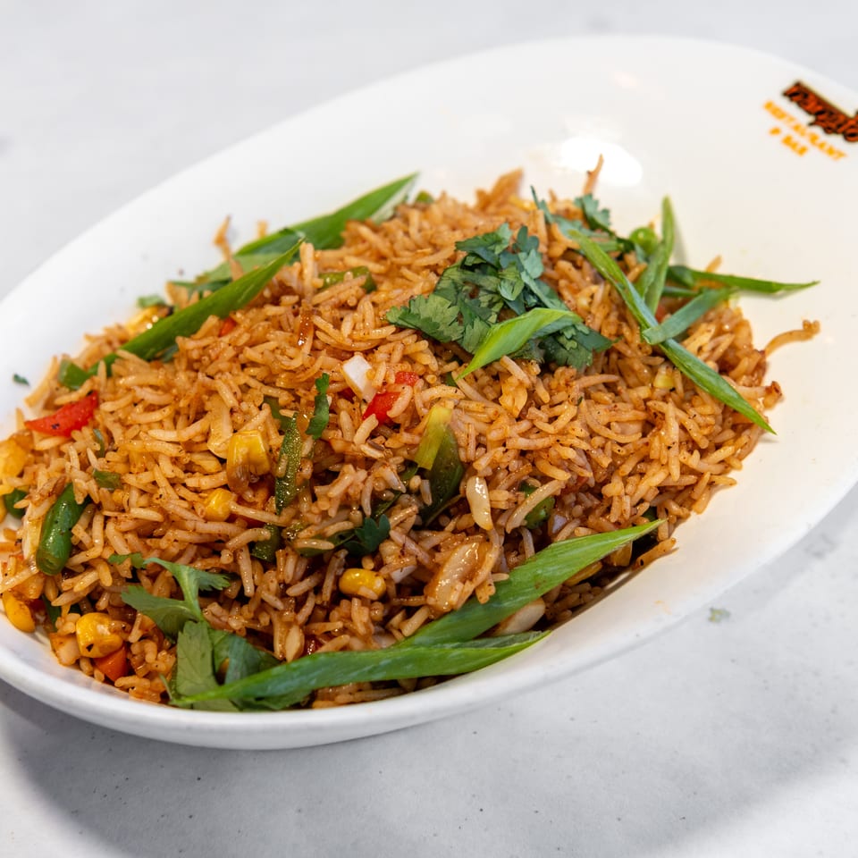 Spiced fried rice with mixed vegetables, cilantro, and green onions served on a white plate.