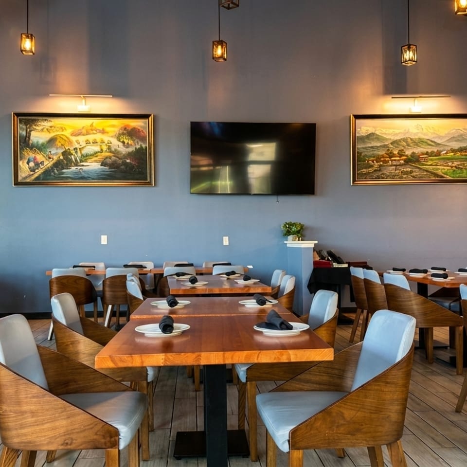 Restaurant dining room with blue walls, wooden tables, light blue chairs, and landscape paintings.
