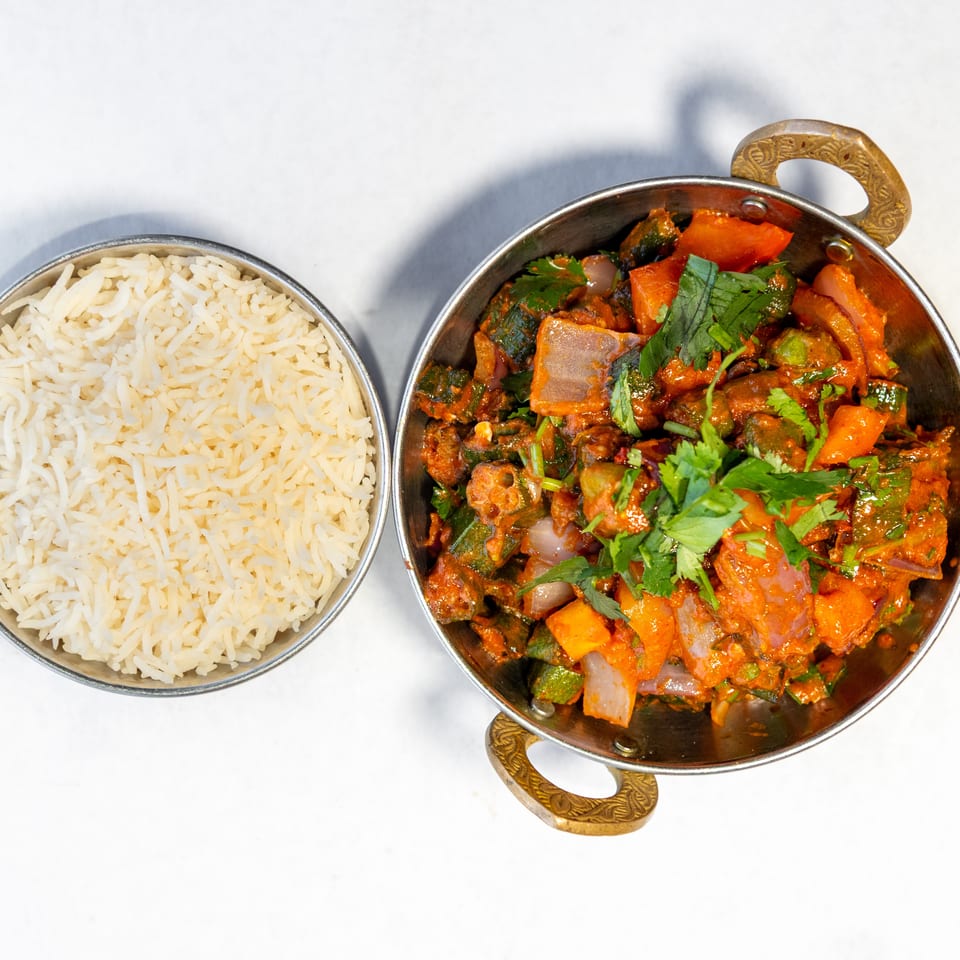Basmati rice served beside a colorful spiced vegetable curry garnished with fresh cilantro in a brass-handled bowl.