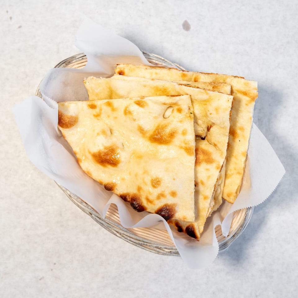 Basket of golden-brown flatbread pieces lined with parchment paper on a light tabletop.