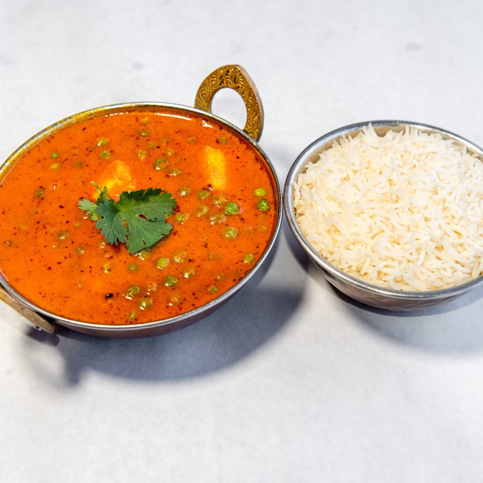 Indian vegetable curry with peas, paneer, and cilantro served beside a bowl of white basmati rice.