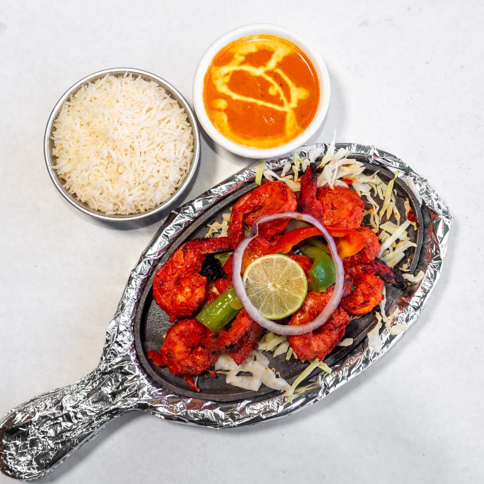 Indian-style sizzling platter with red tandoori meats, peppers, onions, lime, basmati rice, and creamy orange curry.