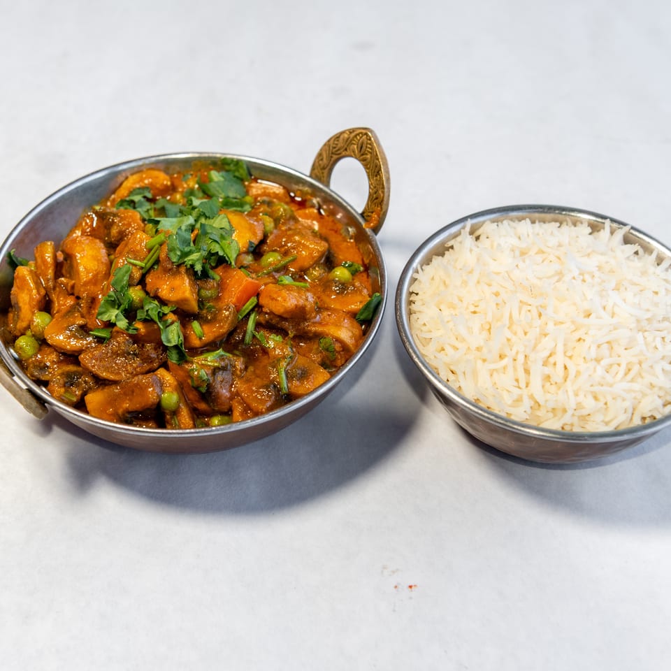 Indian vegetable curry garnished with cilantro and peas in a metal serving dish beside a bowl of white basmati rice.