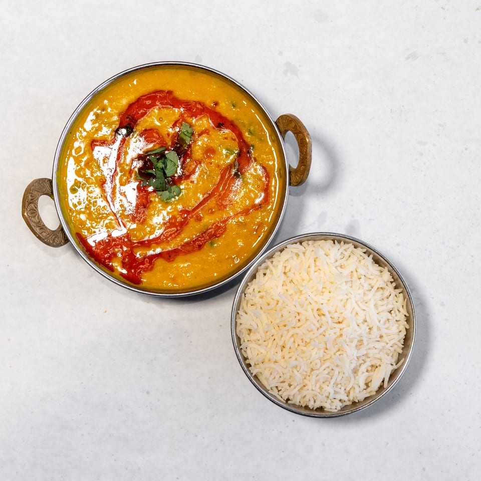 Creamy golden Indian curry garnished with cilantro and red sauce, served beside a bowl of basmati rice.