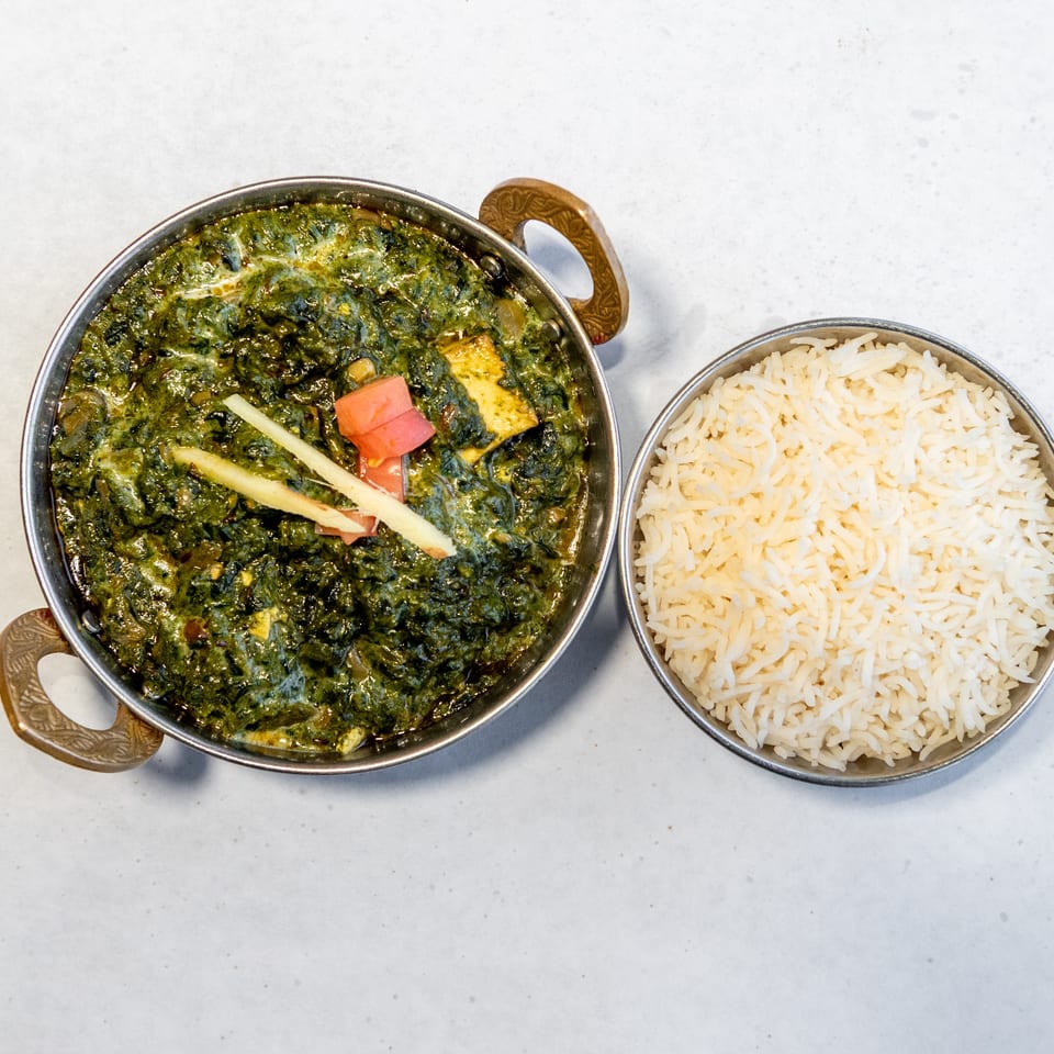 Indian spinach and paneer curry garnished with ginger and tomato, served alongside a bowl of basmati rice.