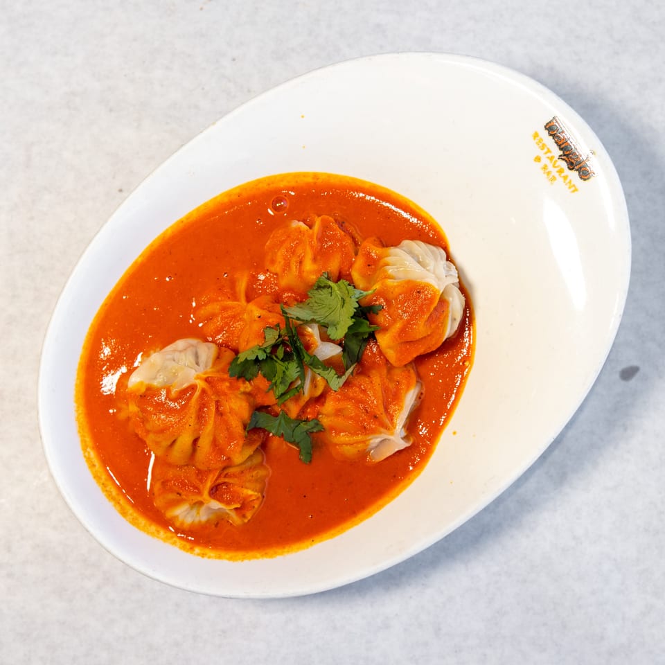 Steamed dumplings topped with cilantro and orange curry sauce, served on a white restaurant plate.